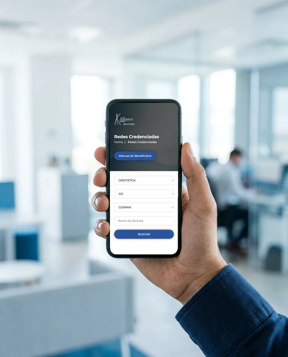 Mão segurando um celular com a busca da rede credenciada da Alliance Odonto aberta: especialidade, estado GO e cidade Goiânia preenchidos